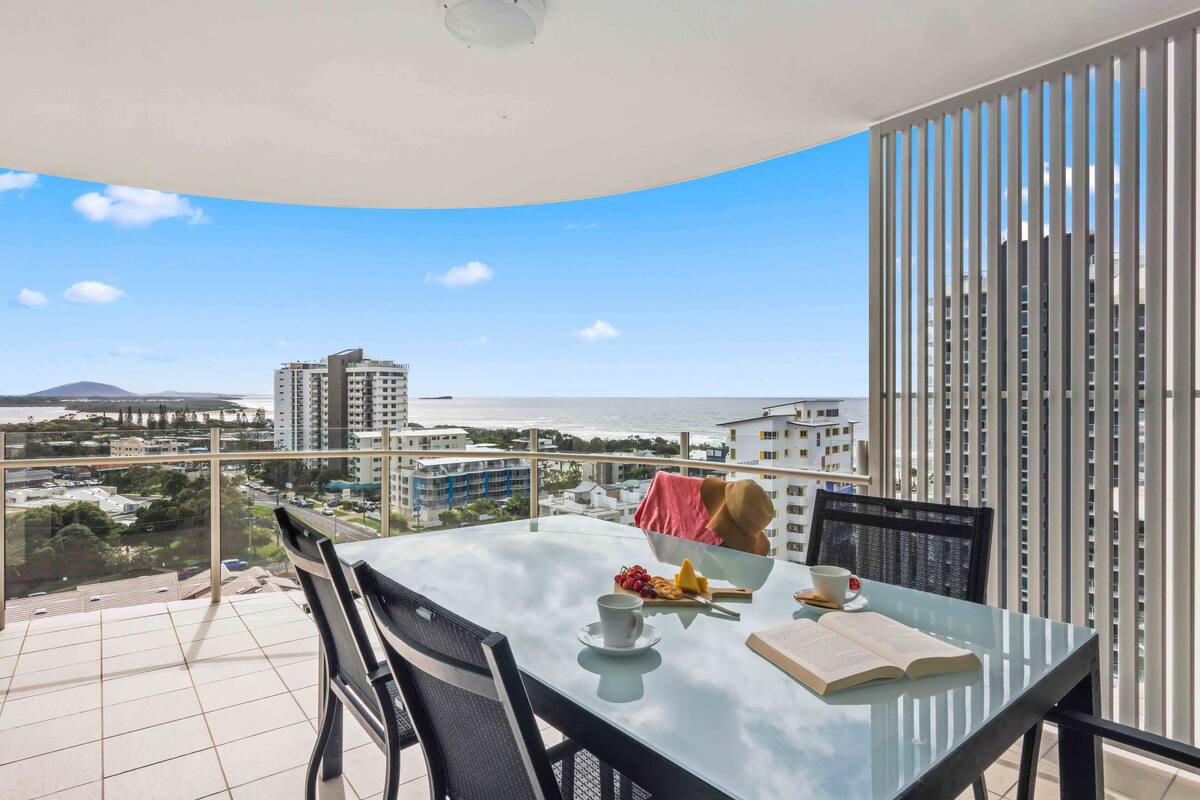 A balcony with a glass table, chairs, and a book.