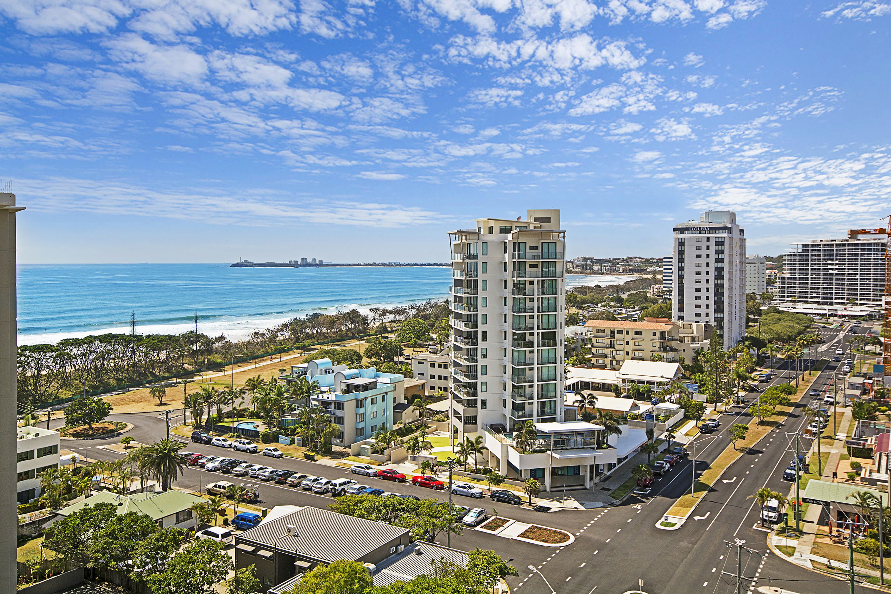 A coastal cityscape with modern buildings, a marina, and a clear view of the ocean.