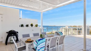 Un porche cubierto con una mesa, sillas, una parrilla y vistas al mar.