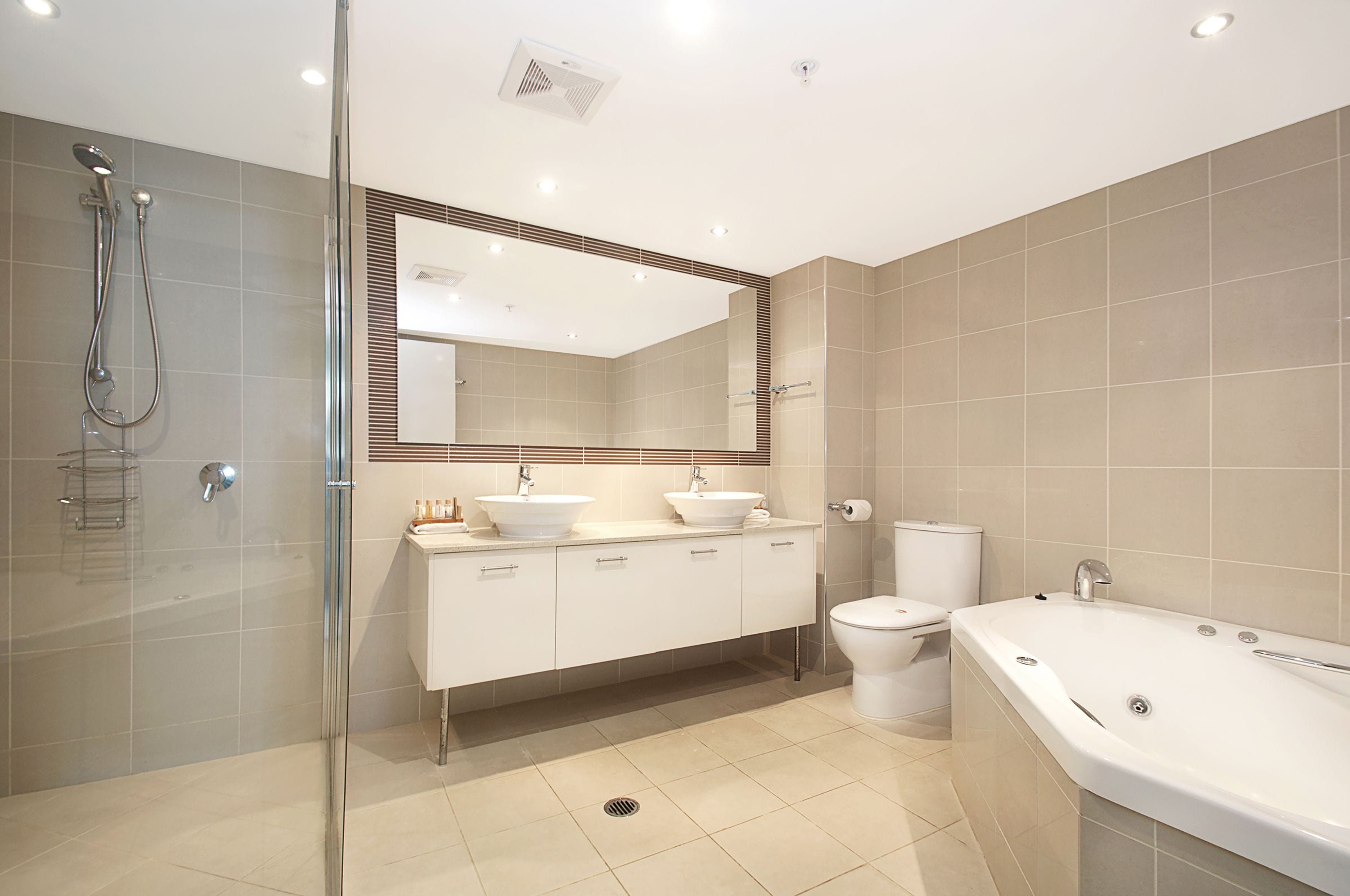 A modern bathroom with a glass-enclosed shower, two sinks, a toilet, and a bathtub.