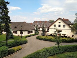 Un edificio de estilo europeo tradicional con un camino adoquinado que conduce a un patio, rodeado de setos y árboles bien cuidados.