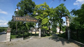 A sign for Hotel Sarmata with a cobblestone path leading to the entrance, surrounded by greenery and a traditional building in the background. - Sarmata (Sandomierz)