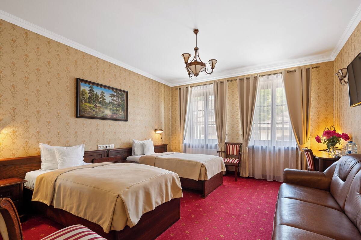 A hotel room with two beds, a red carpet, a chandelier, a painting, and a sofa.