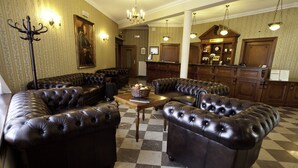 A lobby with leather sofas, a checkered floor, a reception desk, and a chandelier. - Sarmata (Sandomierz)