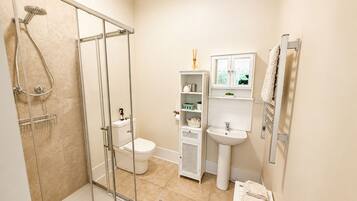 Une salle de bain avec une douche à parois de verre, des toilettes, un lavabo et un meuble-lavabo avec des étagères.
