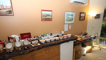 Ein Frühstücksbuffet mit verschiedenen Speisen und Beilagen, ein gerahmtes Kunstwerk an der Wand und Blick ins Freie.