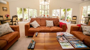 A spacious living room with a large brown sofa, two armchairs, and a coffee table with magazines and remote controls.
