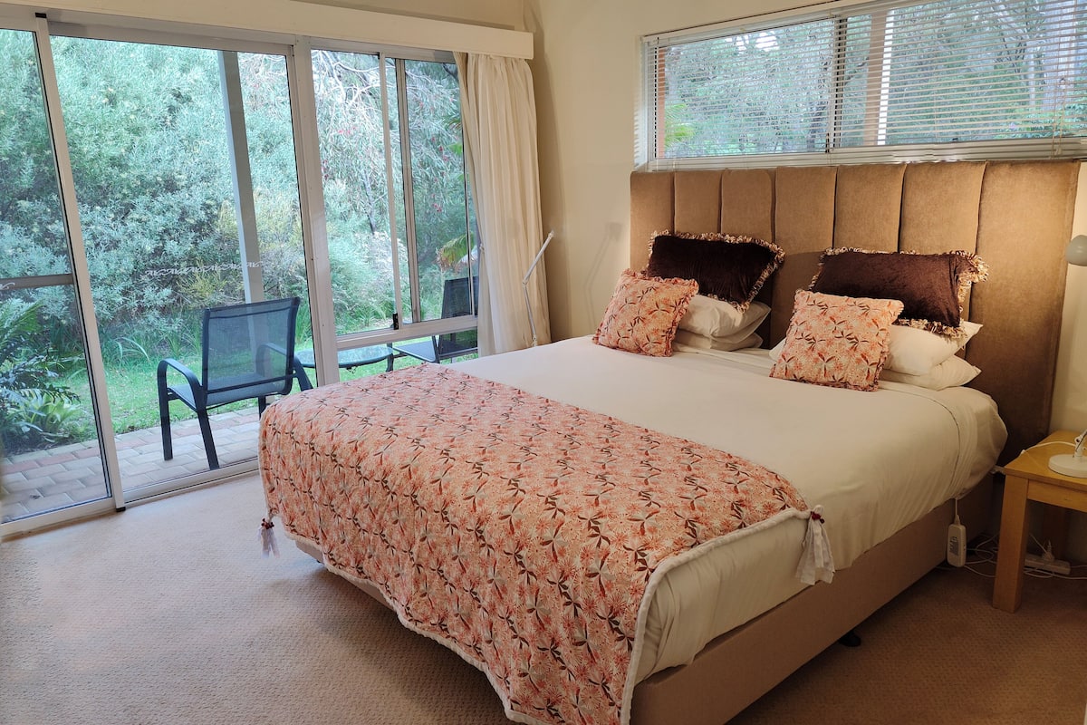 Une chambre à coucher avec un grand lit, une table de chevet, une chaise et une vue sur un jardin par la fenêtre.