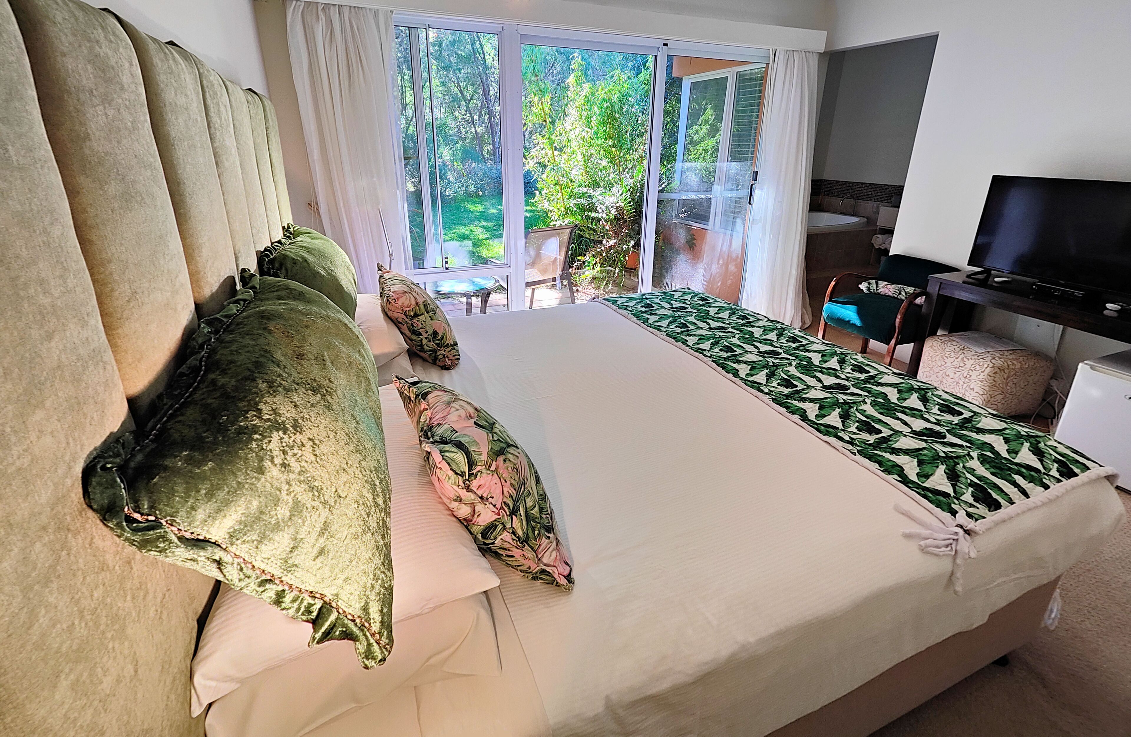 A hotel room with a large bed, a television, and a view of the garden through the sliding glass doors.