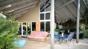 Un patio al aire libre con un sofá de mimbre, una mesa de comedor con sillas y plantas en macetas.