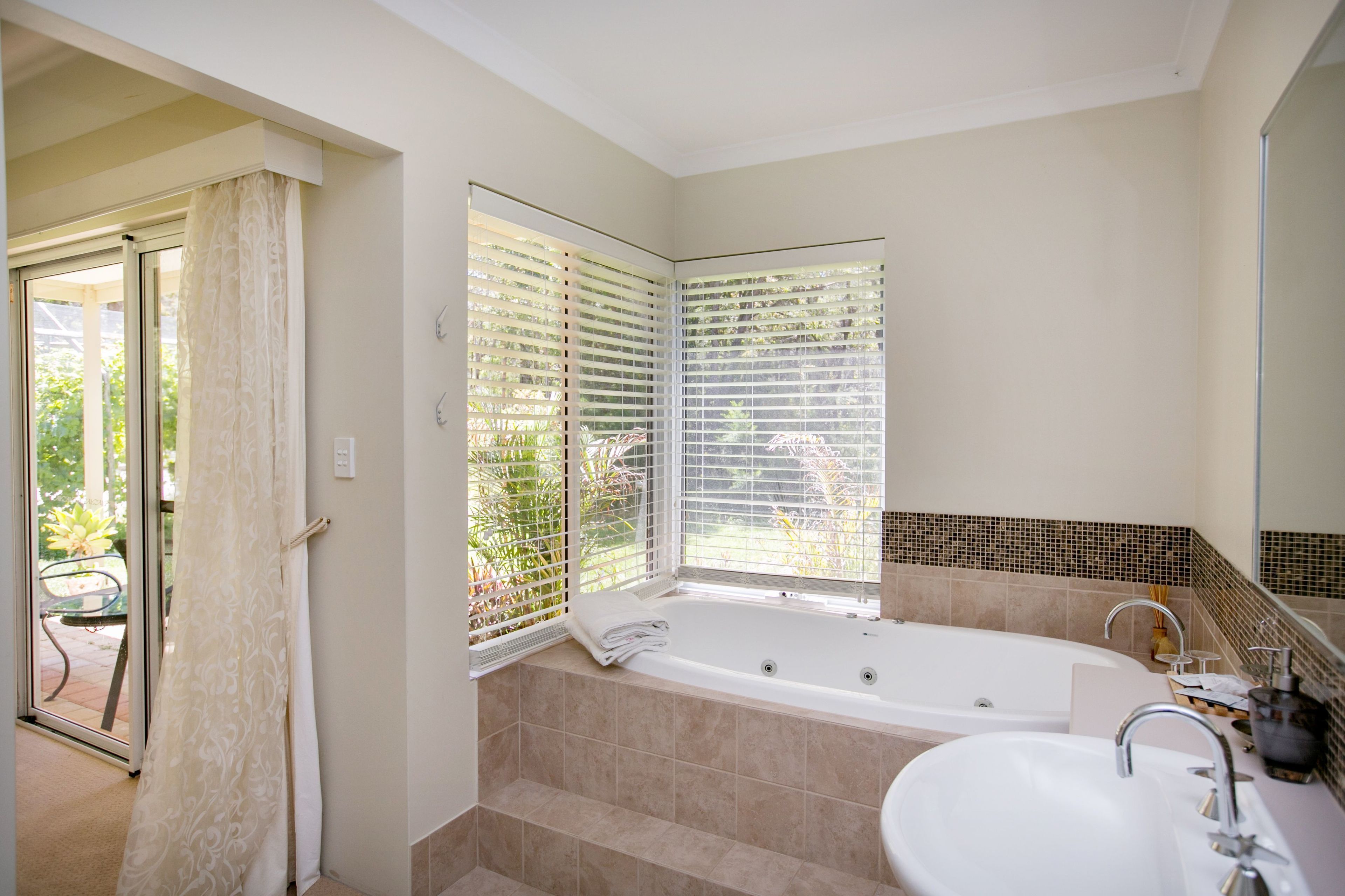 Un baño con bañera, lavabo y ventana con persianas.
