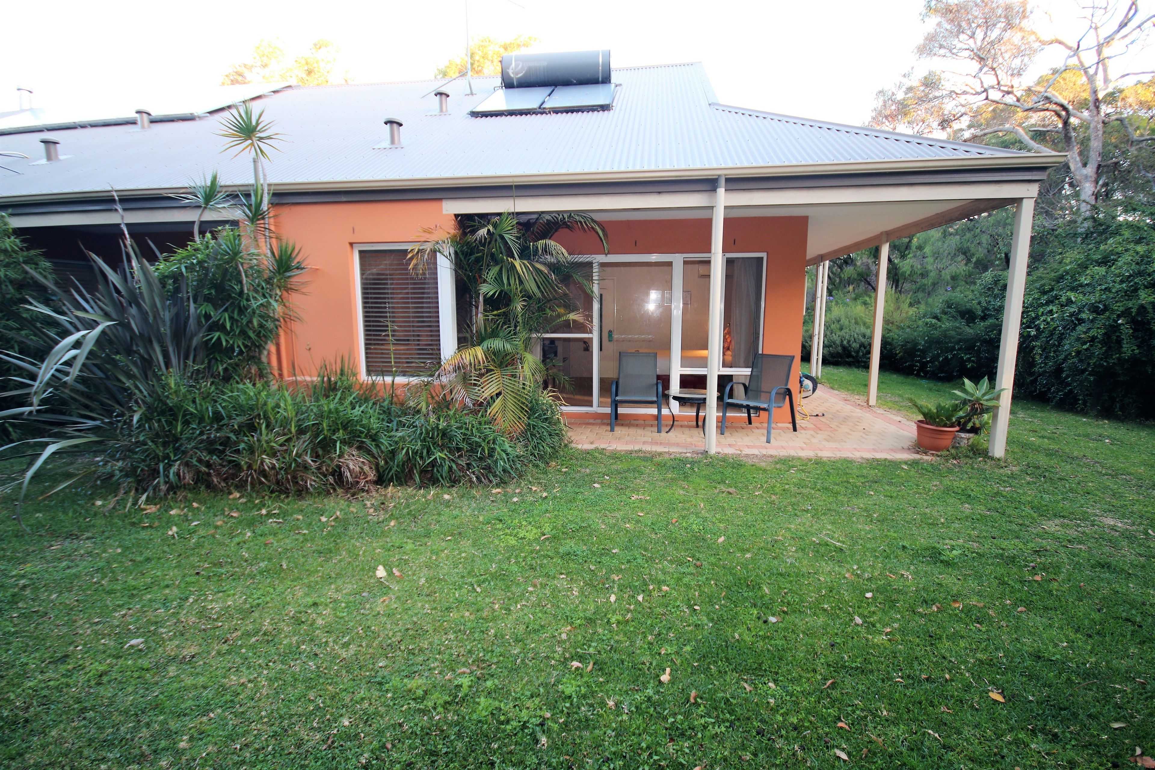 A house with a covered patio, a lawn, and various plants.
