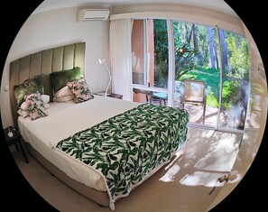 Een slaapkamer met een groot bed, een nachtkastje, een lamp en een raam met uitzicht op een tuin.