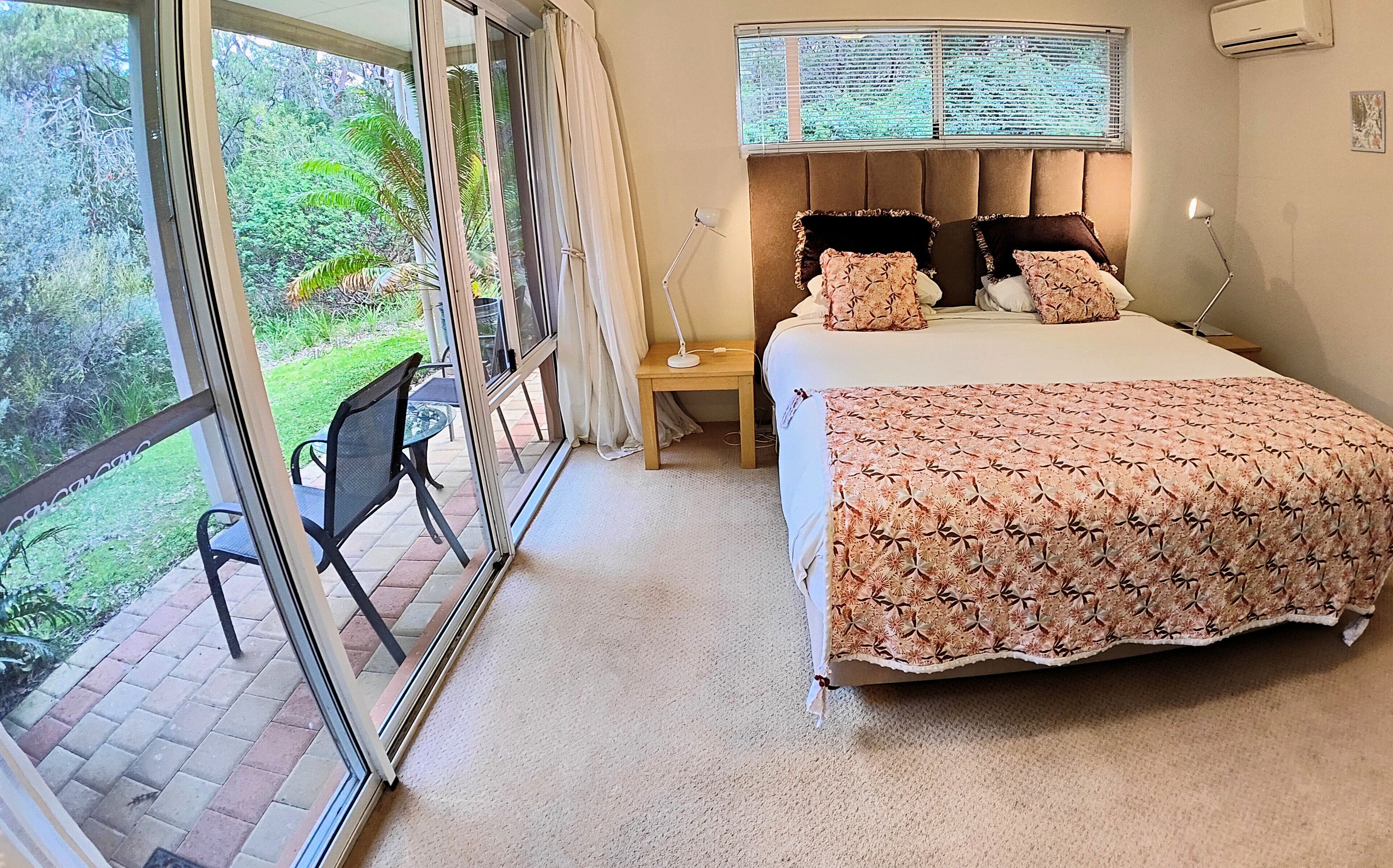 A bedroom with a large bed, a window with blinds, a bedside table, and a chair by the window.