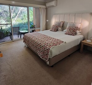 Un dormitorio con una cama grande, una mesita de noche, una silla y vistas a zonas verdes a través de una puerta corredera.