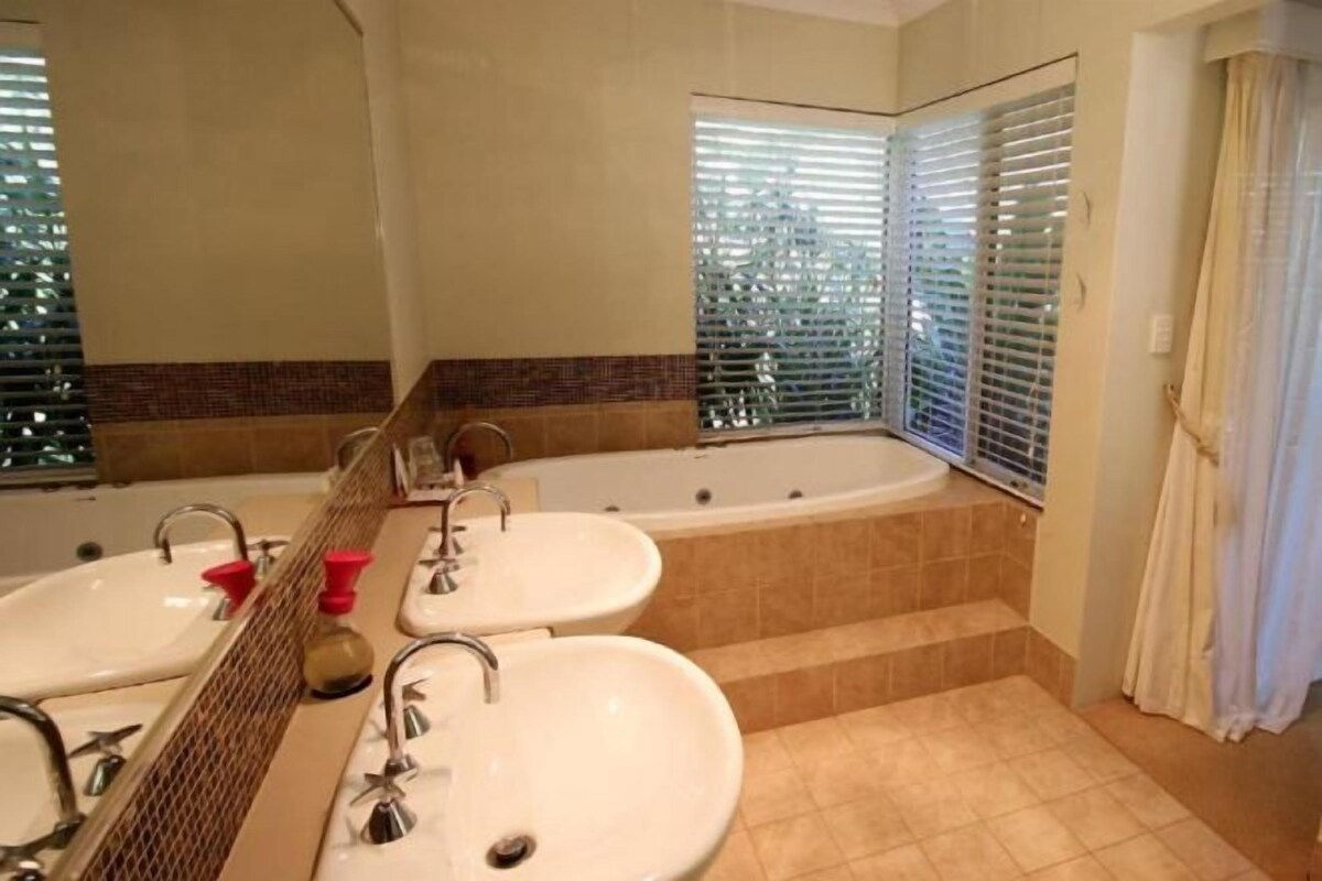 A bathroom with two sinks, a bathtub, and a window with blinds.