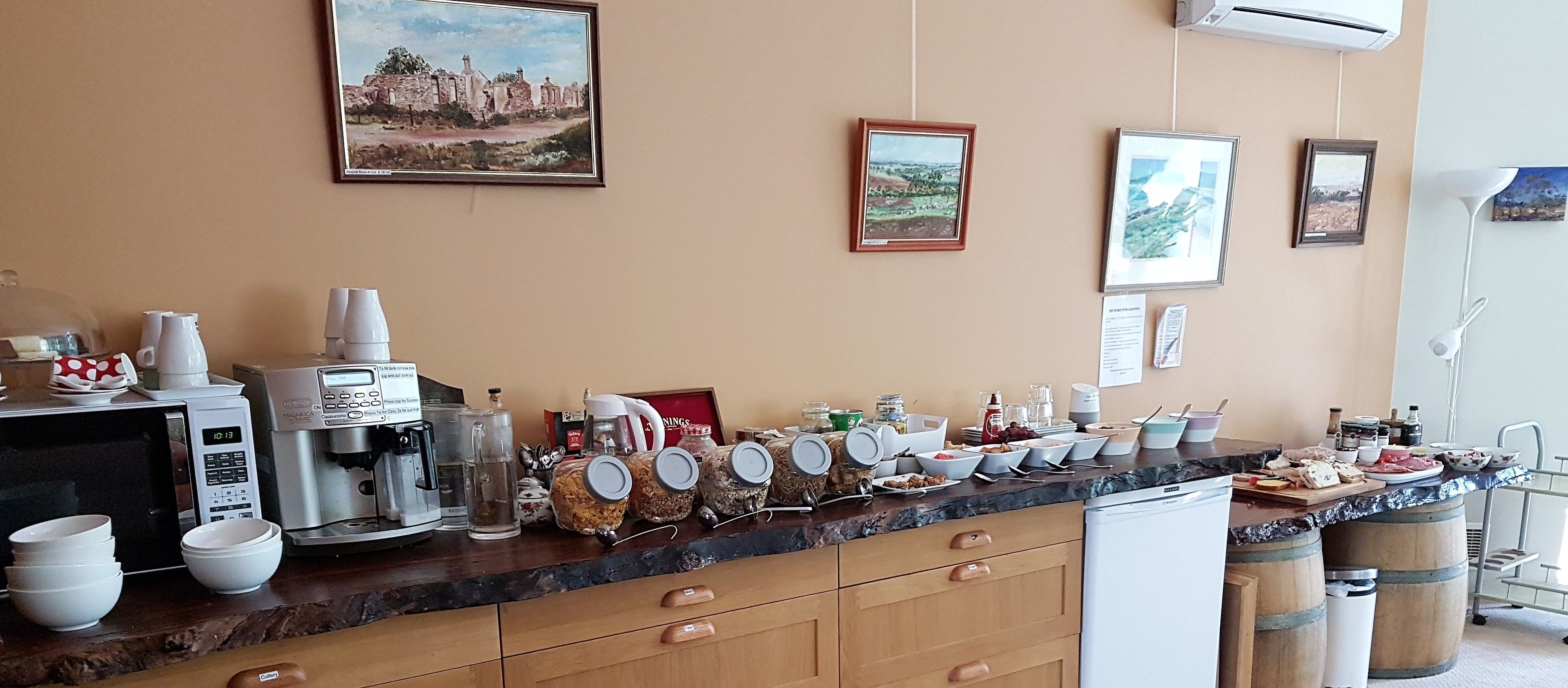 A kitchen with a coffee machine, jars, and a microwave. There are framed pictures on the wall and a sink.