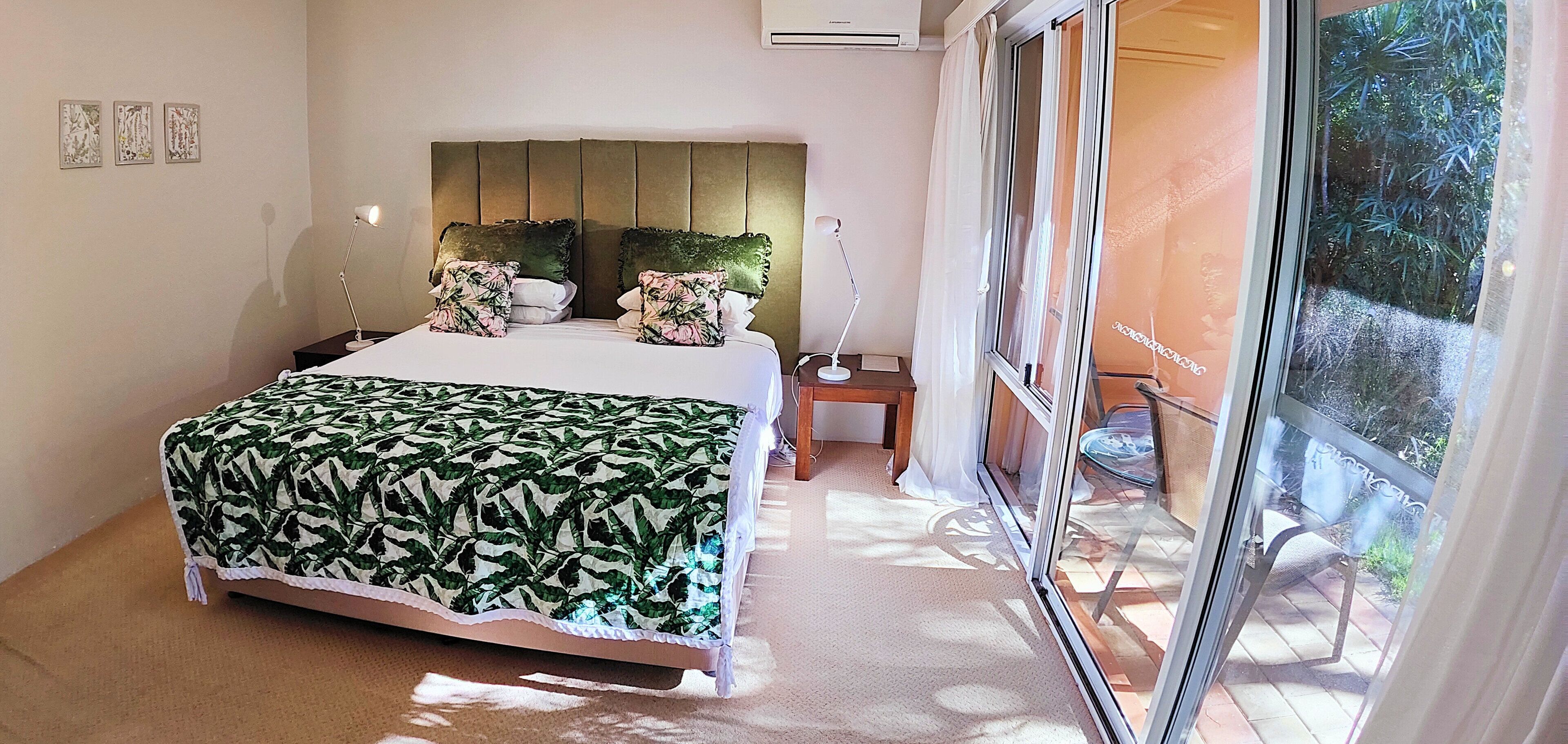 Un dormitorio con una cama grande, una mesita de noche, una lámpara y vistas al exterior a través de una puerta corredera.