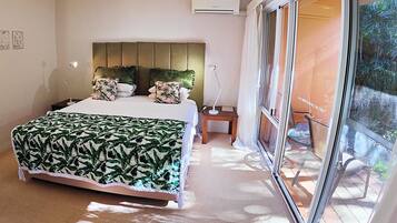 Un dormitorio con una cama grande, una mesita de noche, una lámpara y vistas al exterior a través de una puerta corredera.