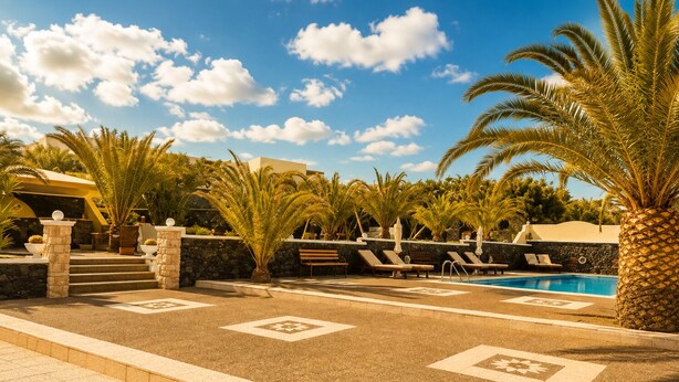A poolside area with lounge chairs, palm trees, and a clear sky. - Villa Danezis (Santorini)