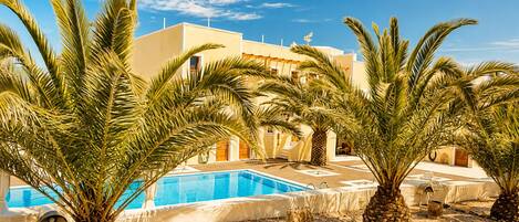 A pool area with palm trees, a clear blue sky, and a building with a flat roof.