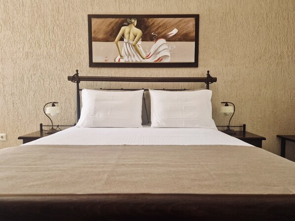 A bedroom with a bed, two bedside tables, and a painting on the wall. - Villa Danezis (Santorini)