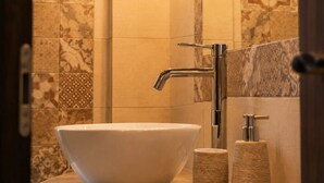 A bathroom with a vessel sink, two wall-mounted lamps, and a hand soap dispenser. - Villa Danezis (Santorini)