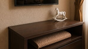 A flat-screen TV mounted on a textured wall above a dark wooden console with a quilted cushion and a white horse-shaped ornament. - Villa Danezis (Santorini)
