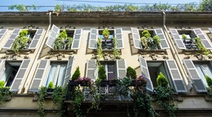 A building with multiple windows, some with shutters, and balconies with plants. - Milanosuites (Milan)