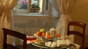 A dining table with chairs, a window with curtains, and a view of a building with flowers outside. - Milanosuites (Milan)