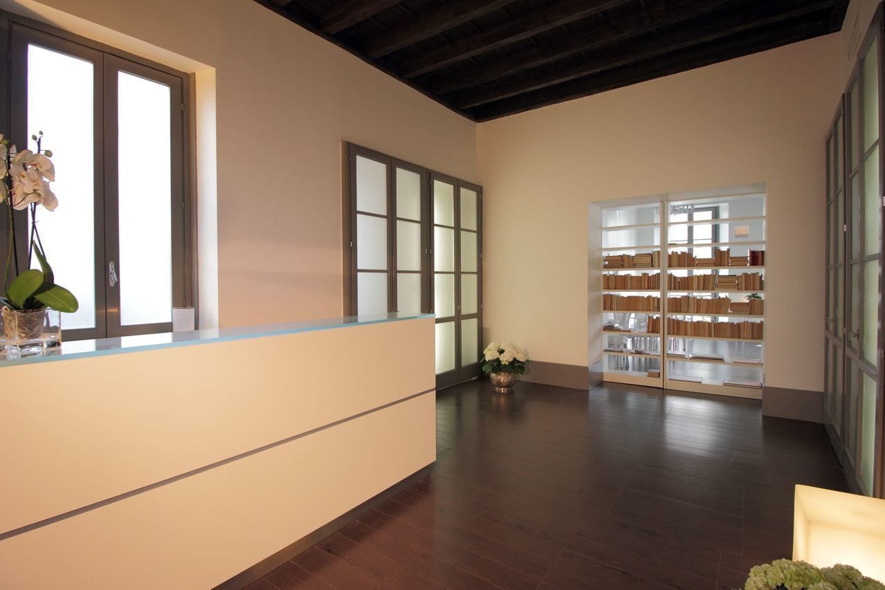 A reception area with a wooden reception desk, a bookshelf, and a large window.