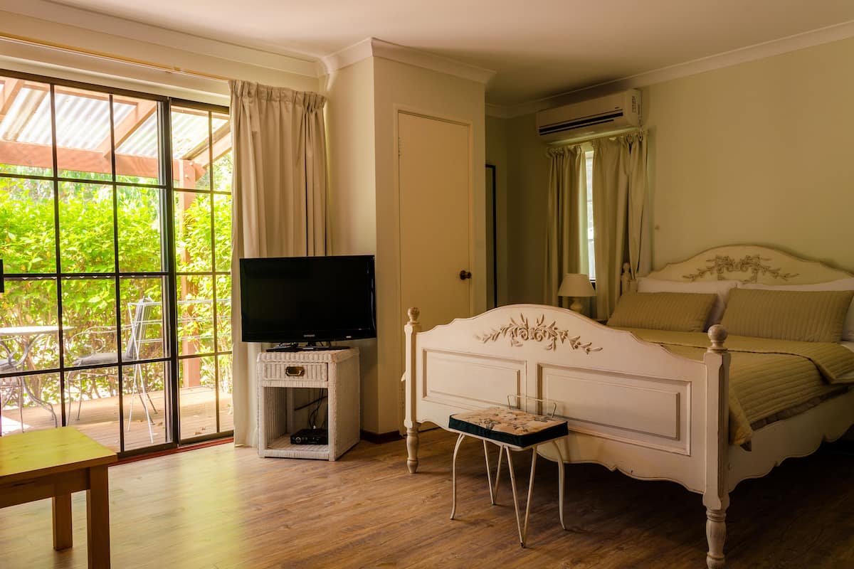 A bedroom with a bed, a television on a stand, and a window with curtains.