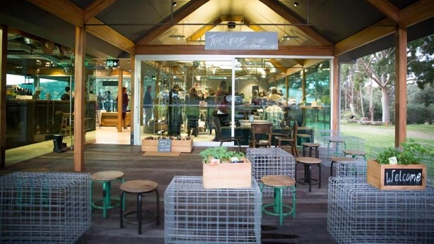 An outdoor café area with wooden beams, glass walls, and seating arrangements including tables and chairs. - Sienna Lodge (Yallingup)