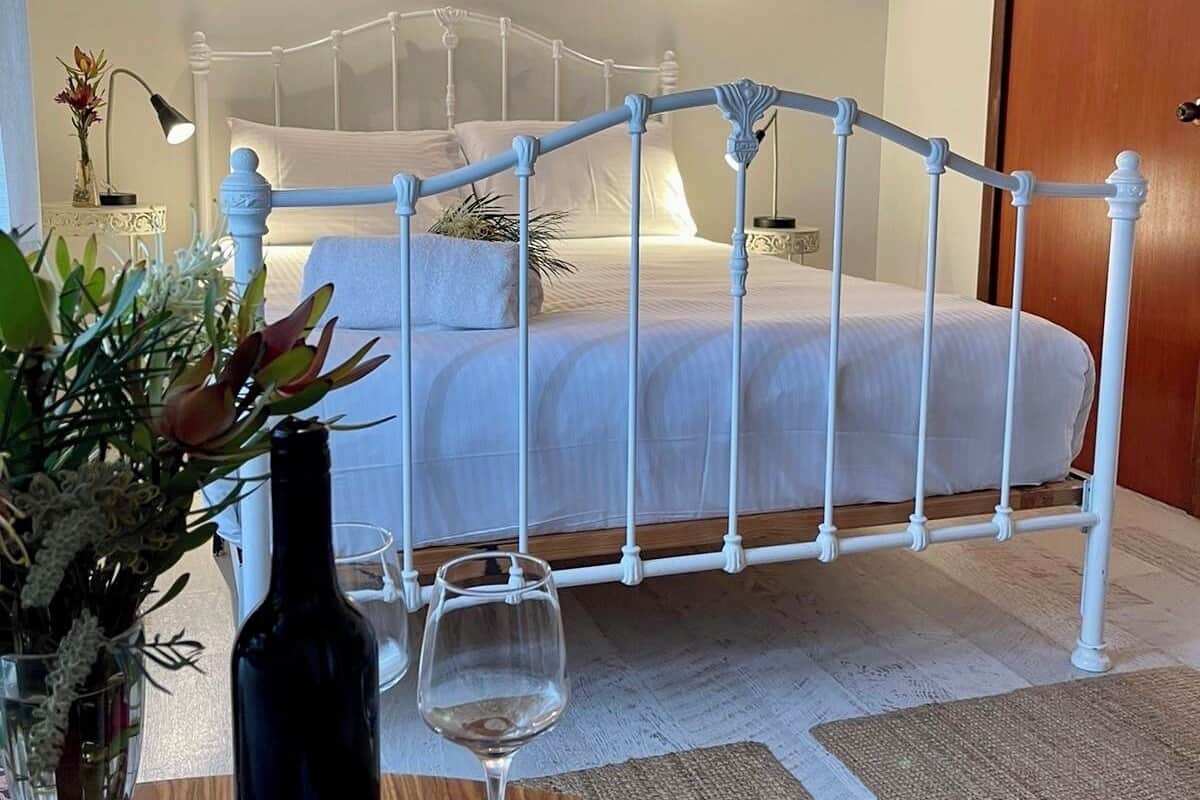 A bedroom with a white metal bed frame, a wooden door, and a nightstand with a lamp and flowers.