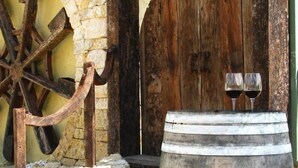 A rustic stone building with a wooden door and steps leading up to it. A large wooden barrel with a tap and two glasses of red wine is in front. - Sienna Lodge (Yallingup)
