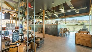 A modern café with a rustic interior, featuring exposed ductwork, wooden shelves, and a bar area with stools. - Sienna Lodge (Yallingup)