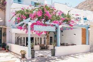 A hotel entrance with a sign reading "Narkissos Hotel," outdoor seating, and potted plants. - Hotel Narkissos (Santorini)