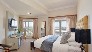 Hotelkamer met een bed, een bureau met een televisie, een stoel, een balkon met gordijnen en uitzicht op de stad.