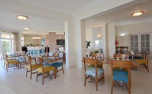 Ein geräumiger Hotel-Speisesaal mit mehreren Tischen und Stühlen, einem Fernseher und einer Küche im Hintergrund.