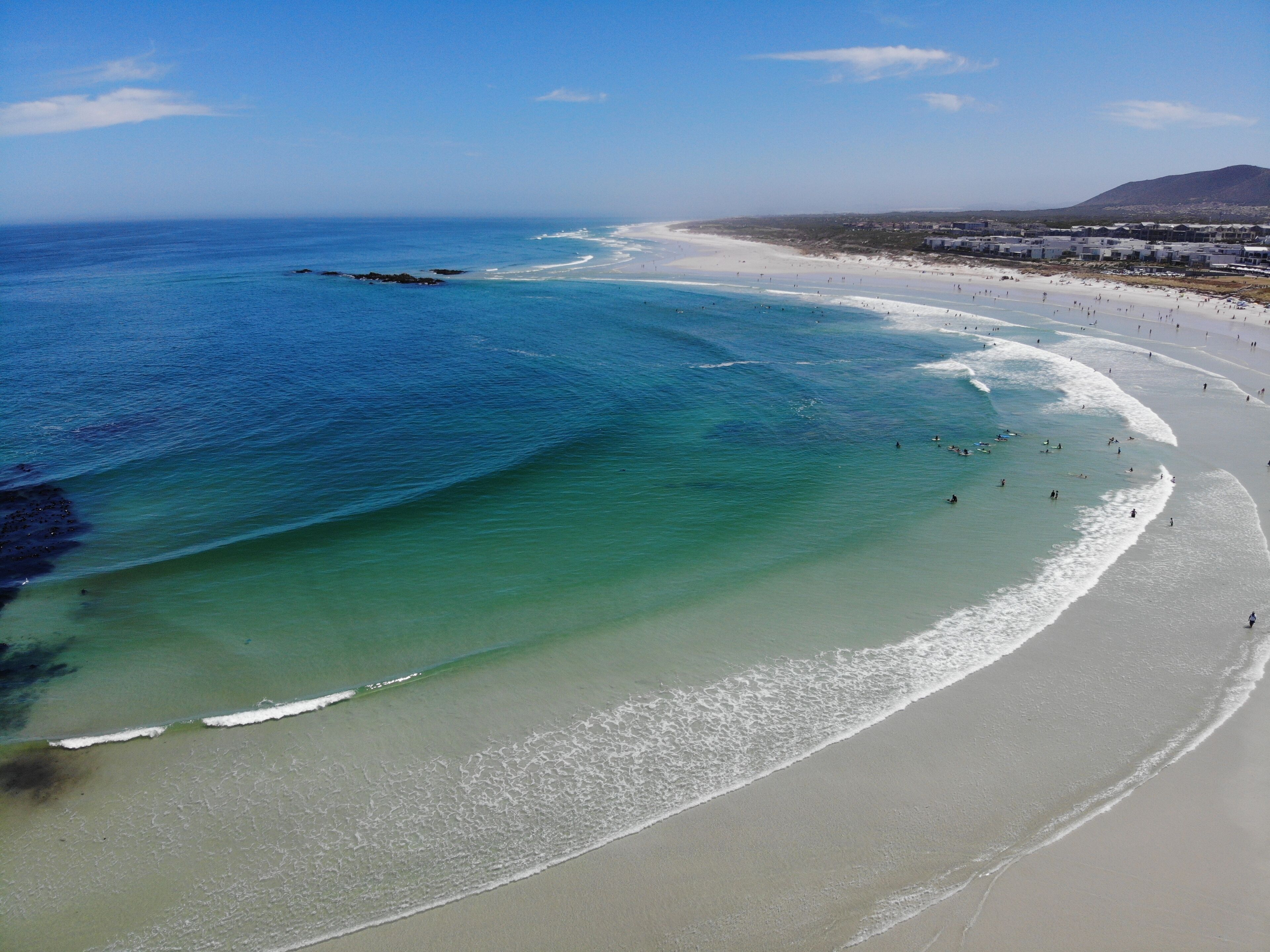 A beach with clear turquoise waters, a wide sandy shore, and a distant mountain range.