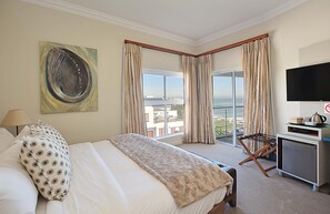 Ein Hotelzimmer mit Bett, Fernseher, Schreibtisch mit Wasserkocher und Balkon mit Vorhängen.