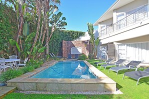 Ein Pool mit Liegestühlen, eine Backsteinmauer und ein Gebäude mit Balkonen.