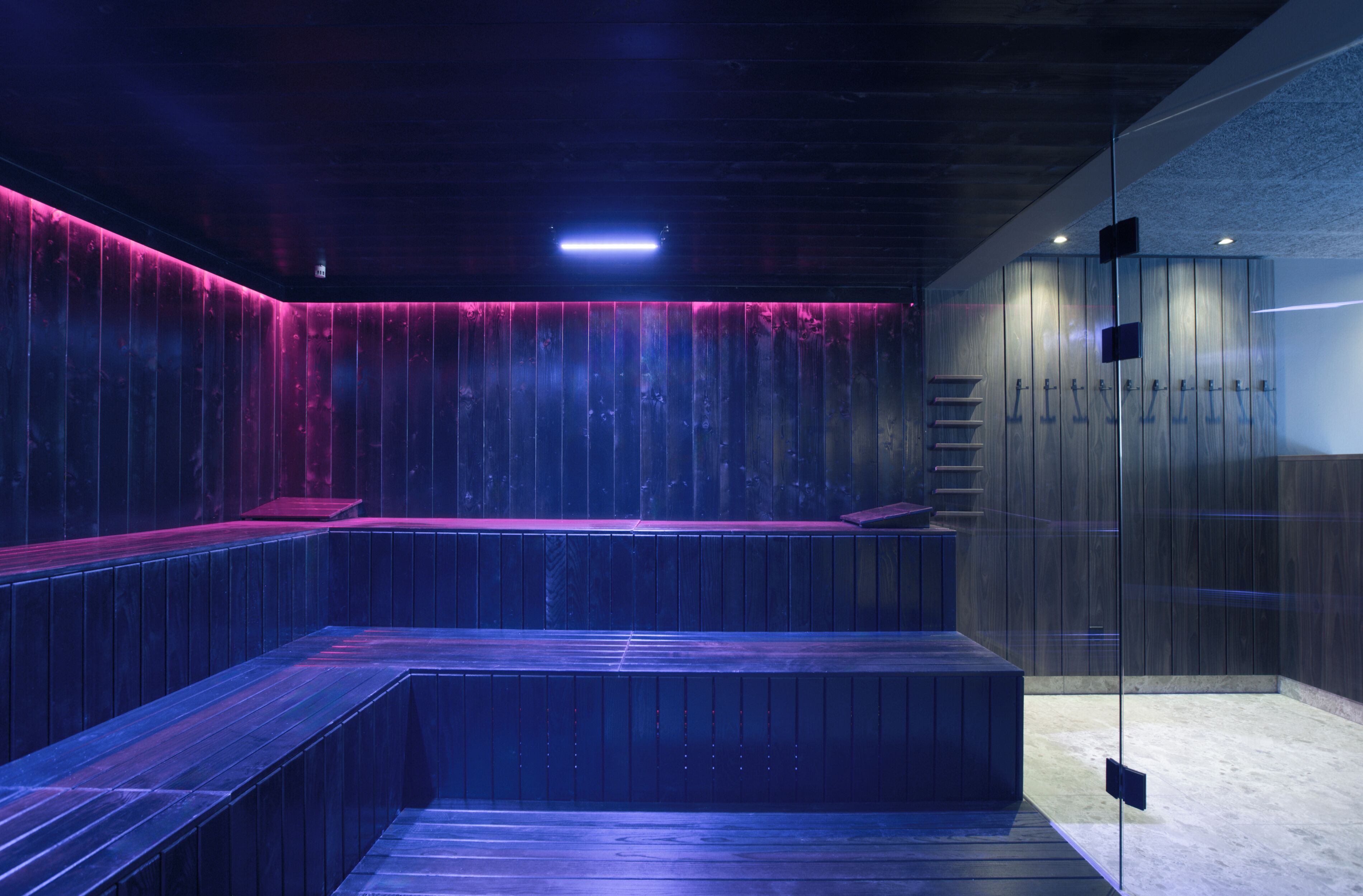 A modern spa area with a wooden bench seating area, a glass partition, and a wooden wall with a vertical light strip.