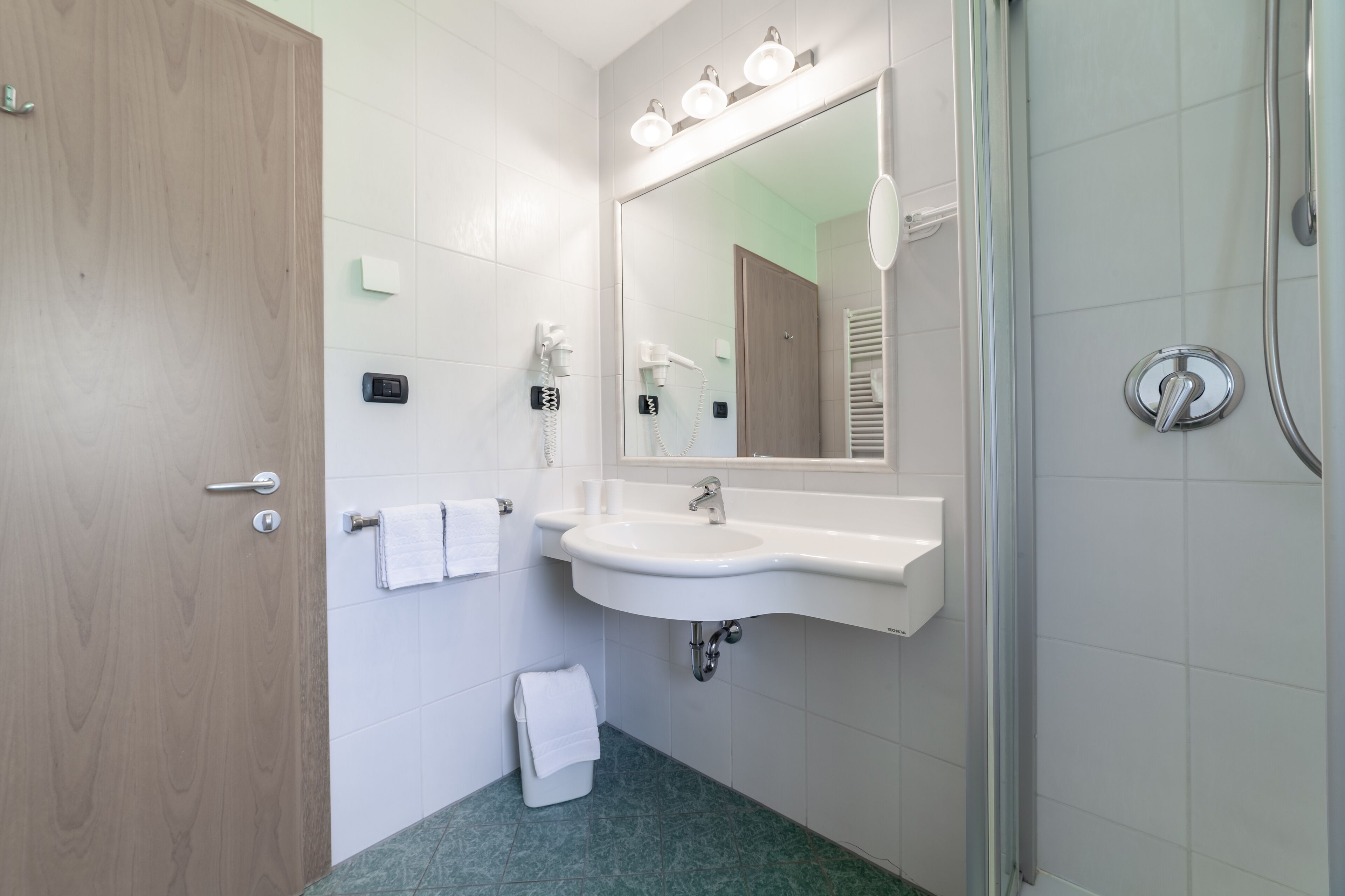 A bathroom with a wooden door, a sink with a mirror above it, a towel rack, and a shower area.