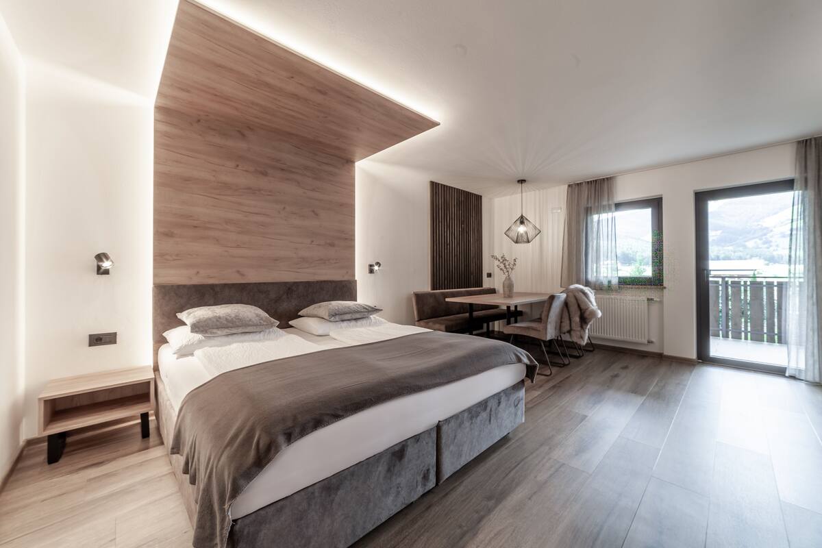 A modern bedroom with a large bed, a desk, and a balcony with a view.
