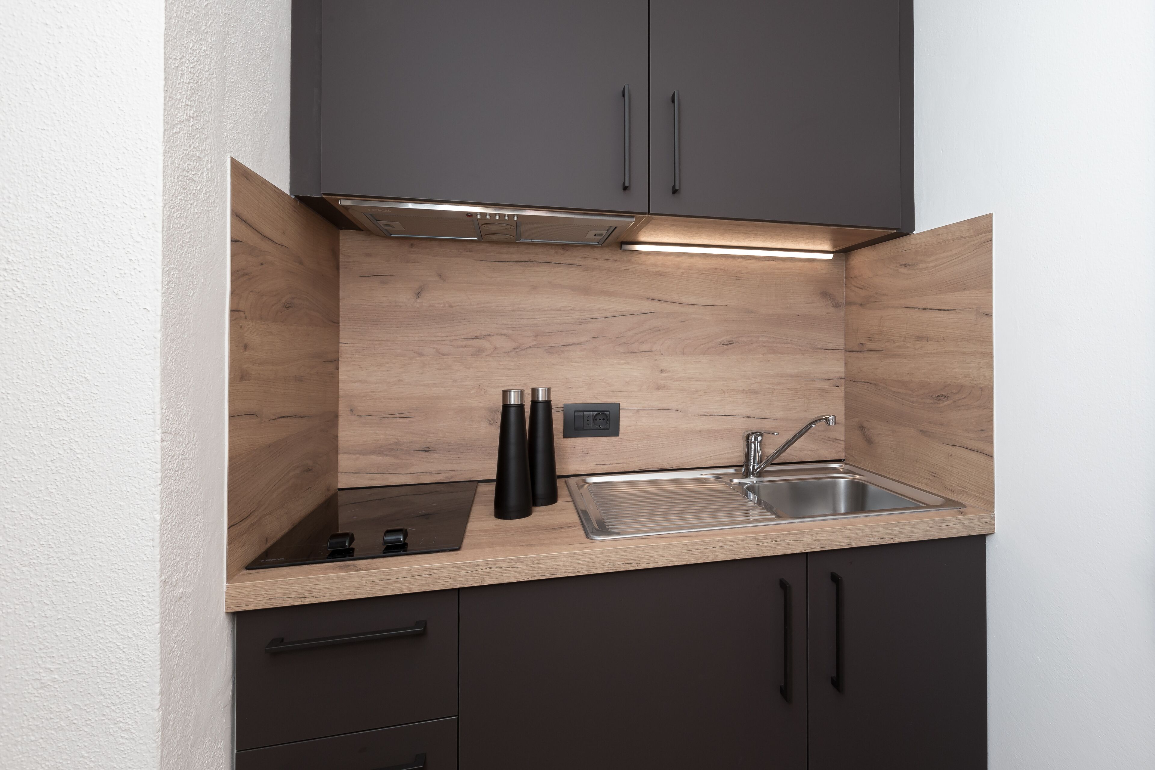 A compact kitchen with dark cabinets, a wooden countertop, a stainless steel sink, and a built-in stove.