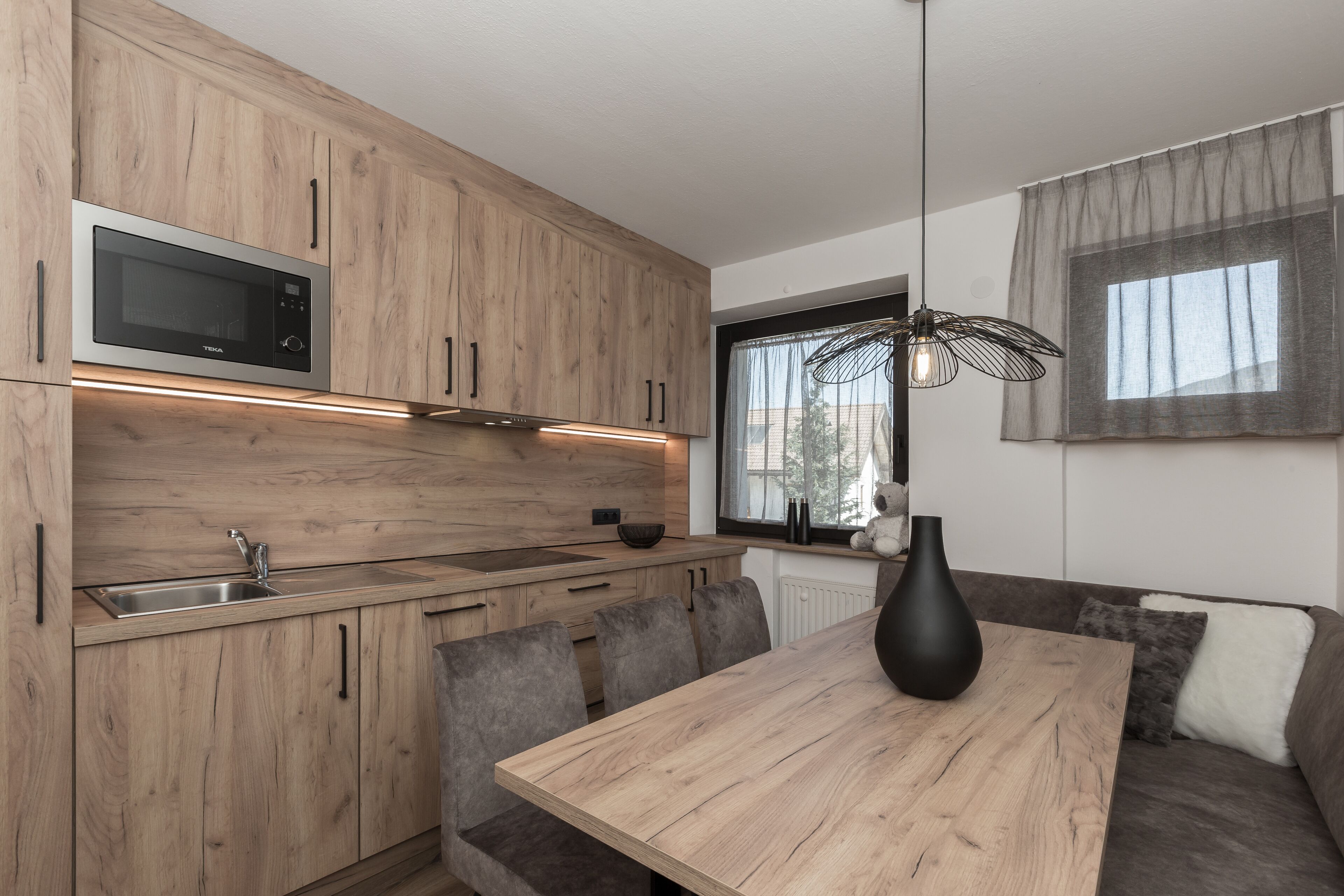Una cocina moderna con armarios de madera, microondas integrado, un lavamanos y una zona de comedor con mesa y sillas.