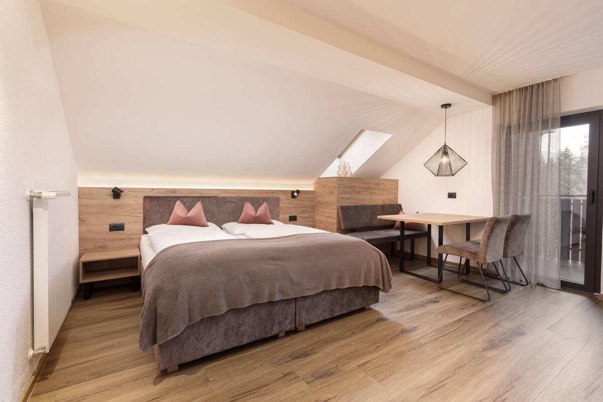 A modern bedroom with a sloped ceiling, a bed with a wooden headboard, a desk, and a chair.