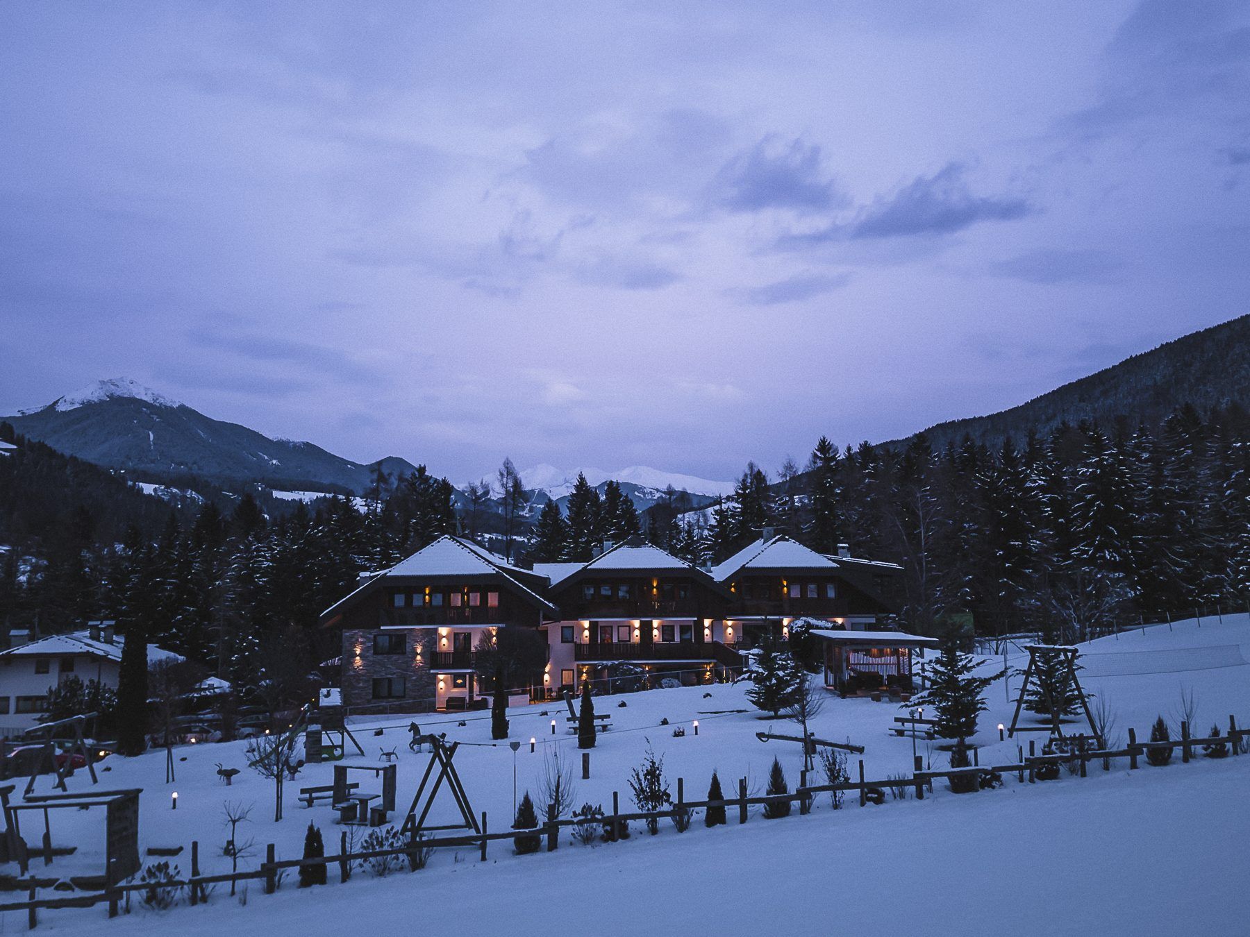 A large lodge with multiple buildings, surrounded by snow-covered trees and mountains.