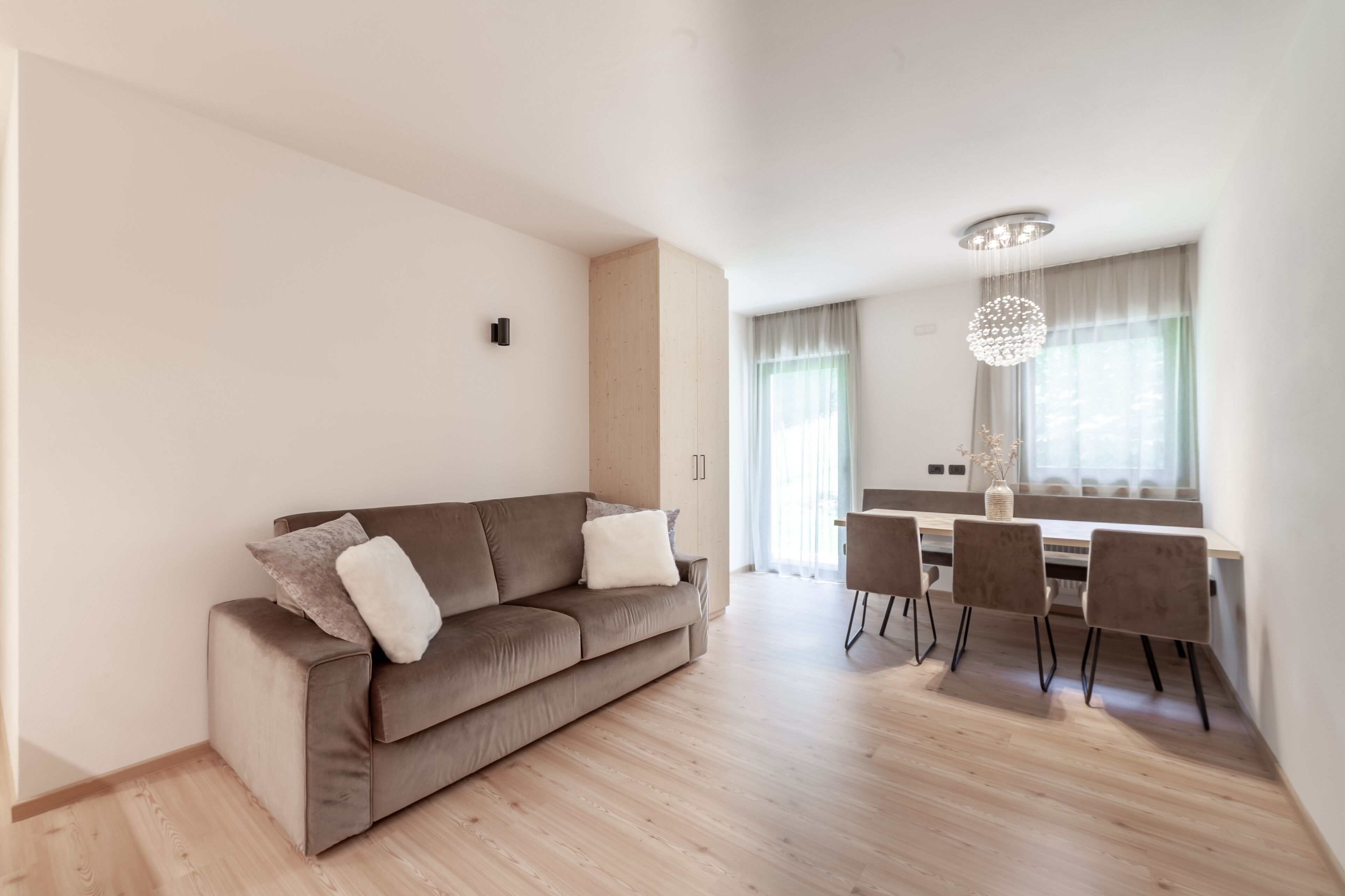 A modern living room with a sofa, dining table, chairs, and a chandelier.